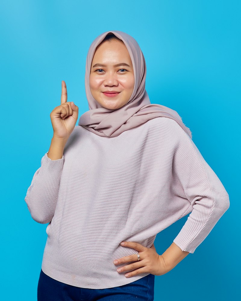 Perempuan berhijab tersenyum sambil menunjuk ke atas