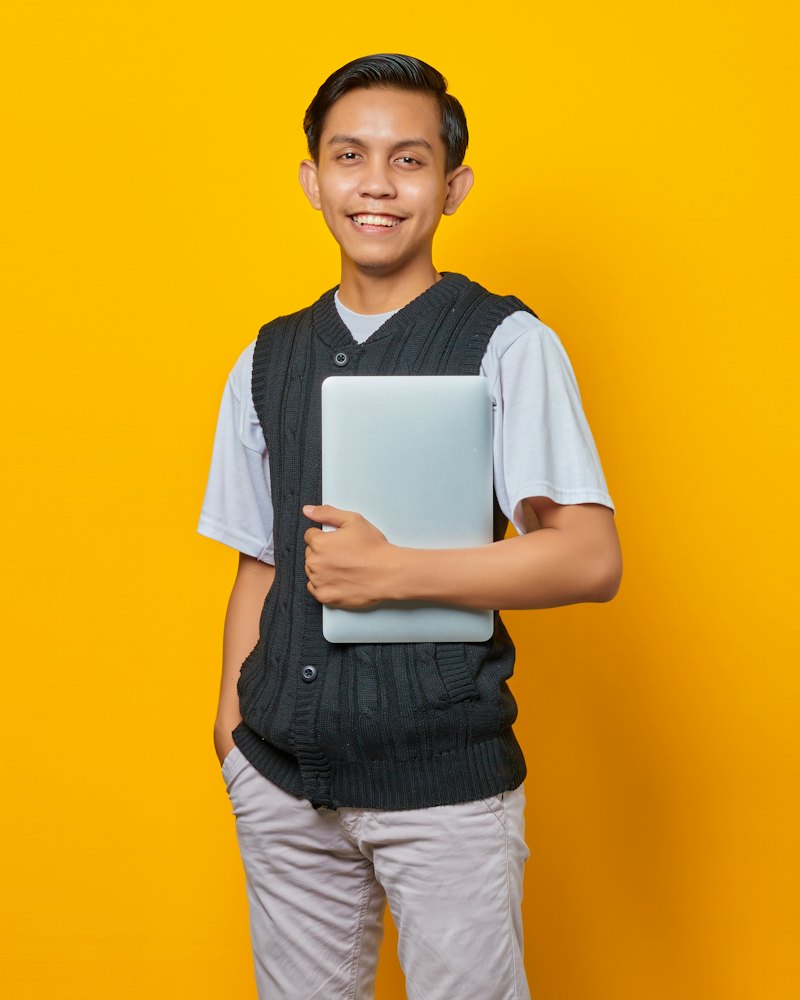 Pemuda tersenyum memegang laptop